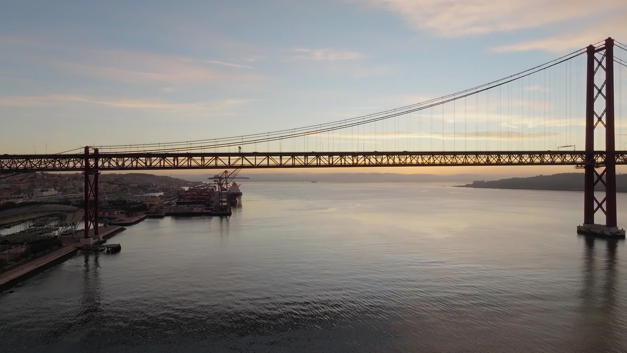 Ponte 25 Aprile che attraversa il fiume Tago all'alba a Lisbona, Portogallo, con ripresa aerea con drone in allontanamento in silhouette mentre un gabbiano si libra in volo