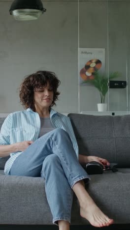 woman relaxing on couch, using phone and listening to music