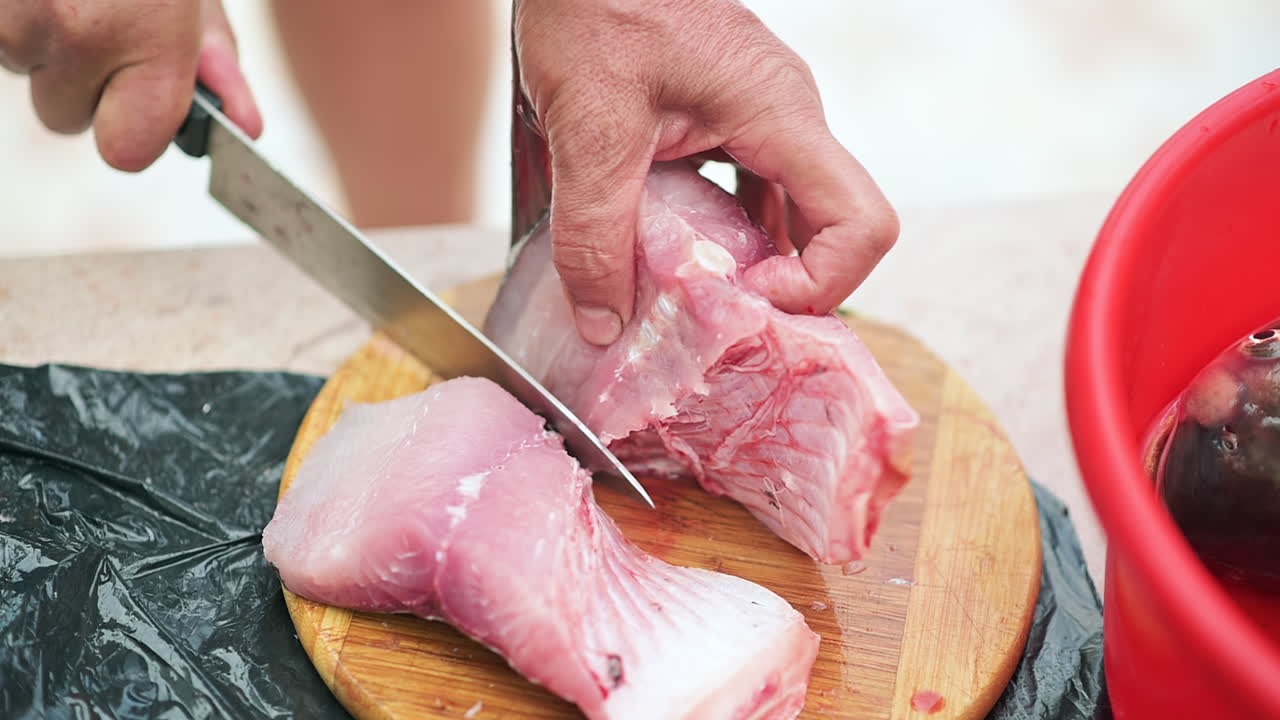 Close up of a man slicing a fish fillet on a wooden cutting board
