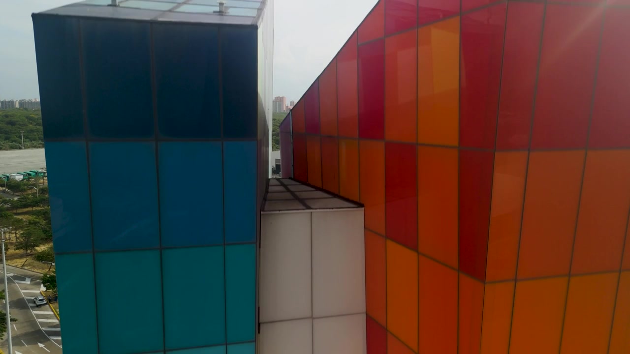 Aerial rising reveal of colorful tile facade on Ventana al Mundo monument with Barranquilla skyline highway and mangroves in tropical Colombia