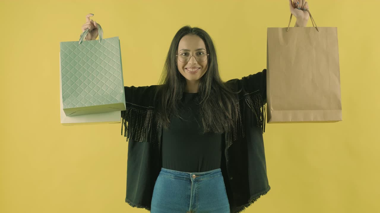joven hermosa con bolsas de compras en el fondo amarillo