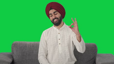hombre indio sikh feliz mostrando la pantalla verde de la señal de ok