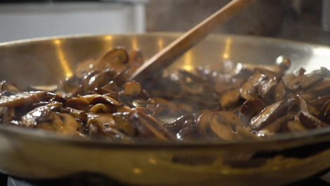 Slowmo-of-stirring,-spreading-mushrooms-with-wooden-spoon,-rack-focus