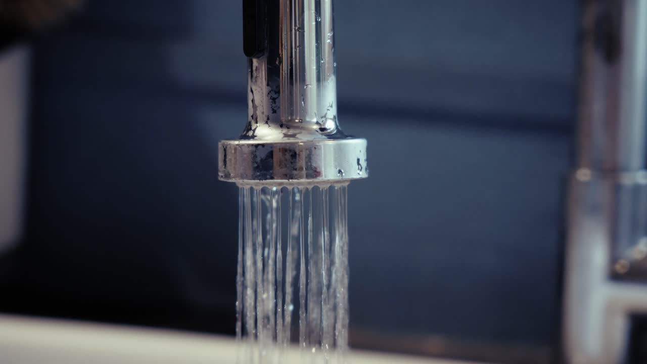 Clear glass being filled with tap water, symbolizing hydration and daily routine, dominant clear and metallic tones in a kitchen environment