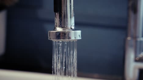clear glass being filled with tap water, symbolizing hydration and daily routine, dominant clear and metallic tones in a kitchen environment