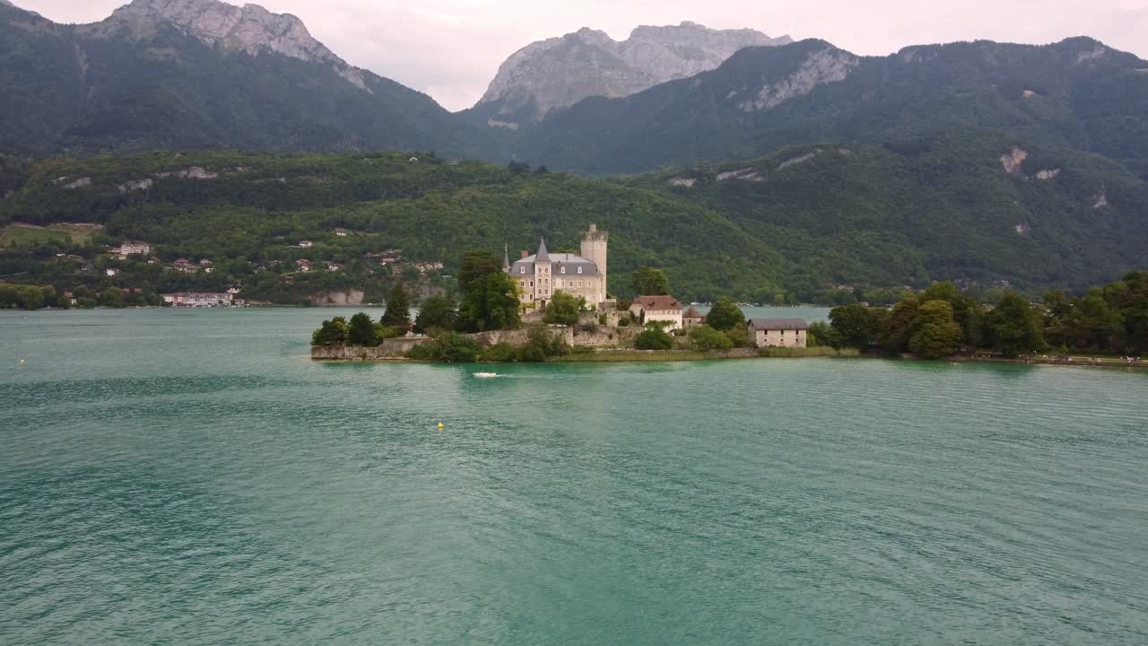 Drone footages flies low towards and sleight rotates on Château de Duingt an amazing castle sticking out on Lake Annecy in Southern france. Beautiful mountain background behind