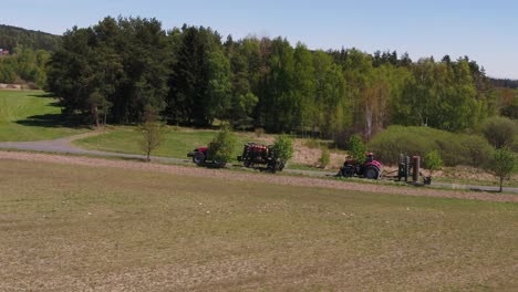 drone semi orbit showing agricultural machinery resting beside field and tree line on a sunny spring day