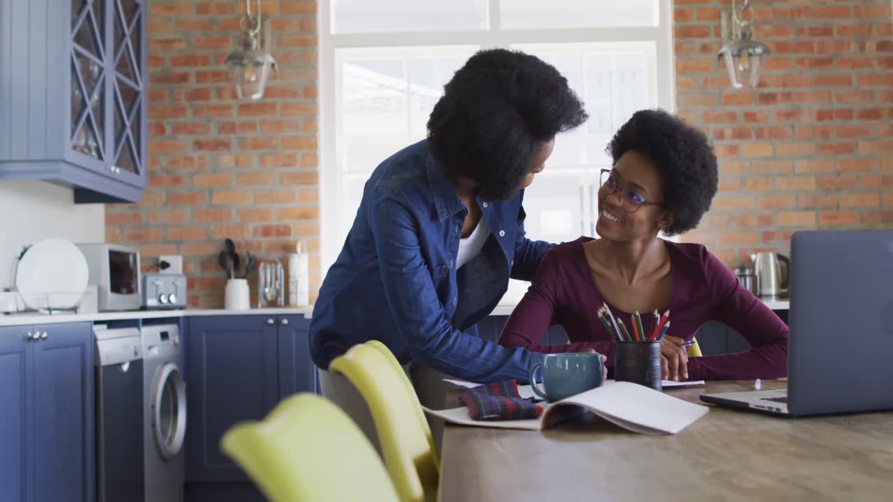 Happy african american mother and daughter doing homework together in kitchen