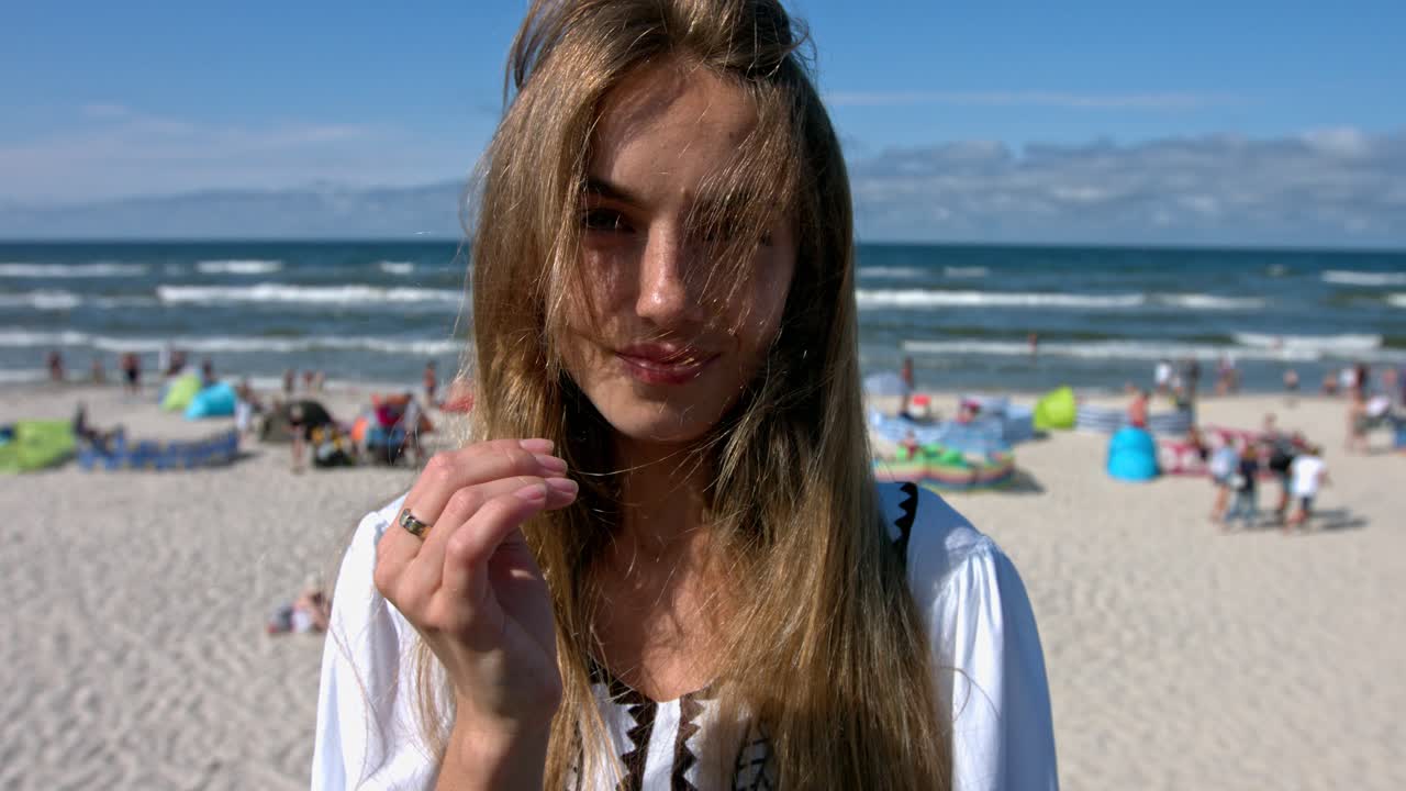 Beautiful young woman standing on the sunny beach full of turists.