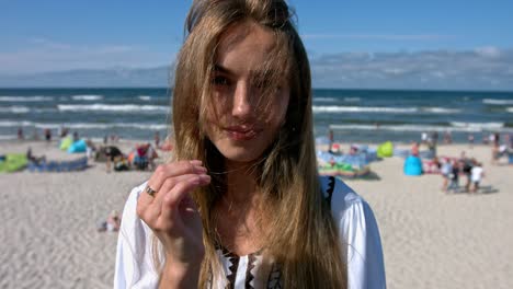 beautiful young woman standing on the sunny beach full of turists.