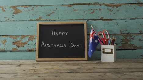 Texto-Del-Feliz-Día-De-Australia-Y-Bandera-Australiana-Con-Estrellas-Y-Artículos-Escolares-En-Una-Mesa-De-Madera