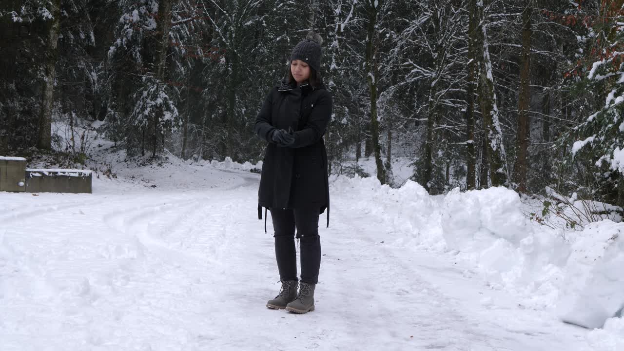 검은 가죽 장갑을 끼고 겨울 풍경에 손을 비비는 여자
