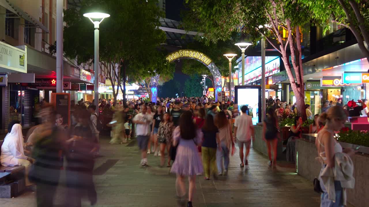 Bustling downtown Brisbane city with massive crowds of people paced in Queen Street Mall, featuring the iconic landmark archway in the background, influx of population, night time-lapse shot.