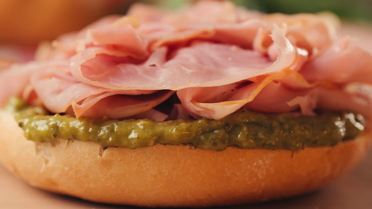 Mortadella ham sandwich, Traditional italian focaccia filled with thin pesto slices of mortadella, served by chef man in cafe restaurant. Macro of traditional italian spanish tapas antipasti.