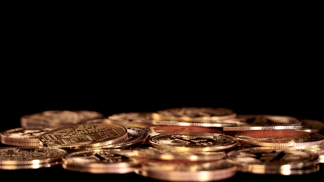 A golden digital currency token drops onto stacked coins under dramatic studio lighting, static shot