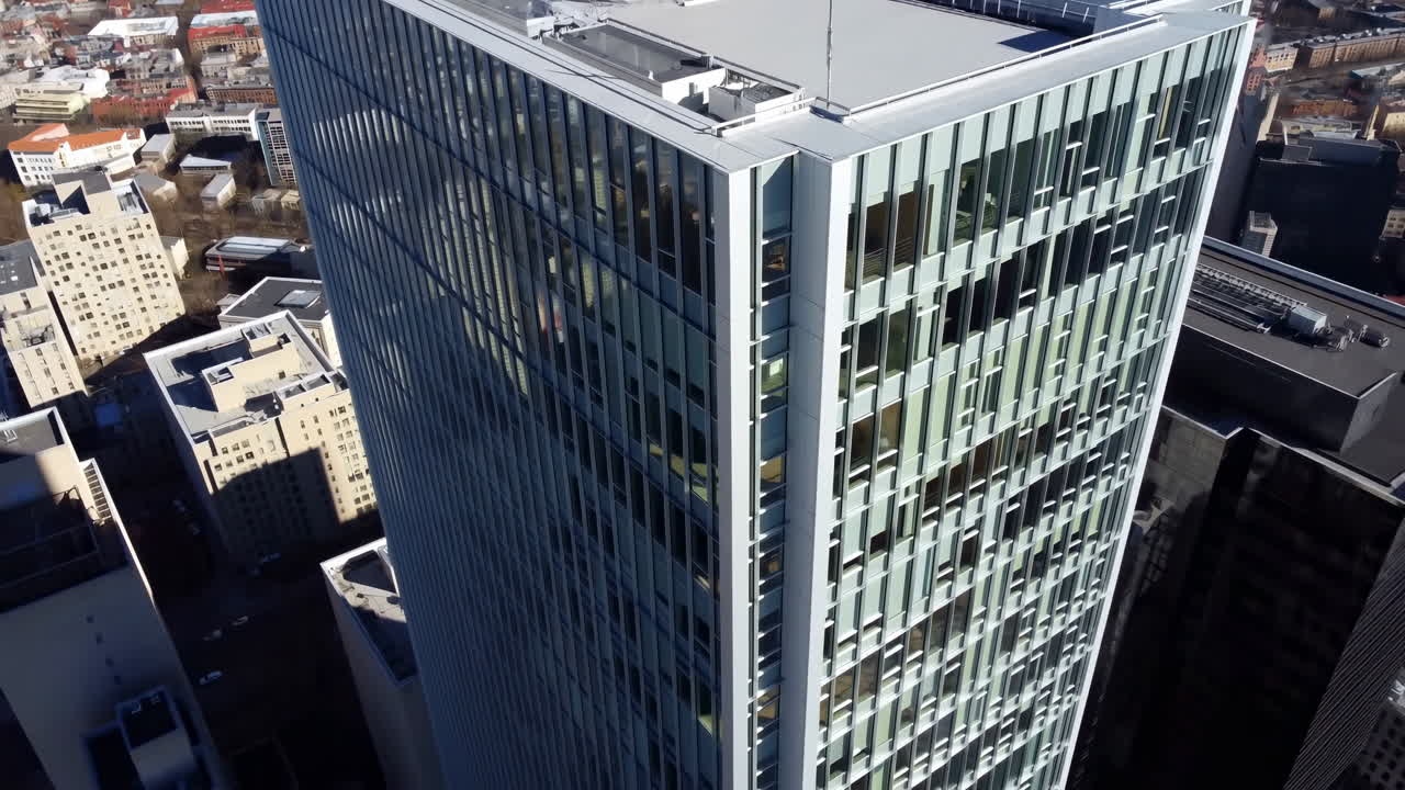 Vista aérea con dron de un rascacielos moderno de cristal mostrando su fachada reflectante, las instalaciones mecánicas de la azotea y los alrededores.