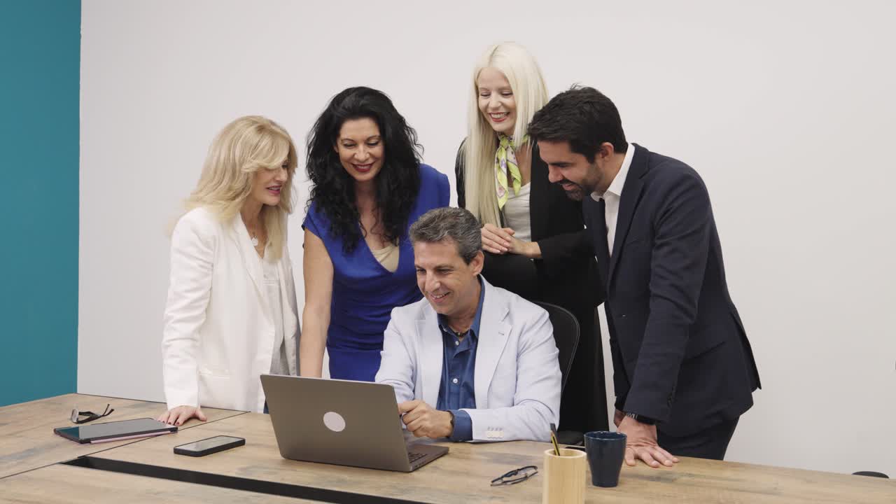 Team aziendale eterogeneo che collabora e sorride intorno a un laptop in ufficio