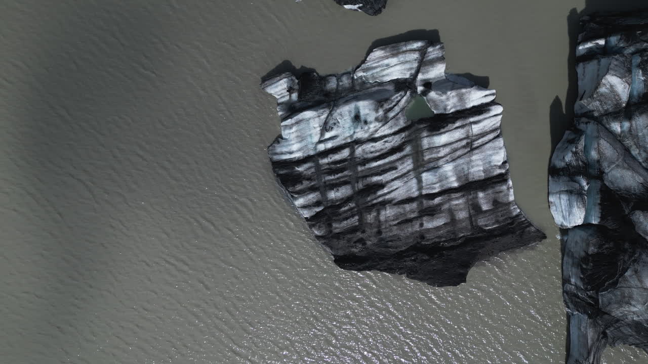 Aerial top down of rocky glacier at glacial lake in summer. Volcanic landscape in Iceland. Flyover shot