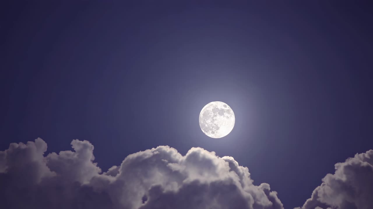 A serene night sky video captures a full moon shining brightly above fluffy clouds, shot from a low
