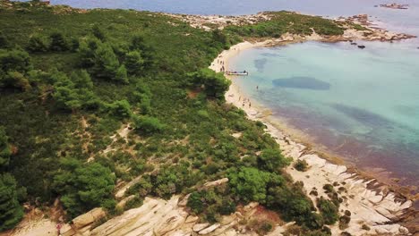 Aerial-drone-shot-transcending-and-cinematic-tilt-down,-on-a-beautiful-beach-with-turquoise-waters-and-some-people-in-the-distance-enjoying-leisure-time-on-the-sun,-Halkidiki,-Greece-4K