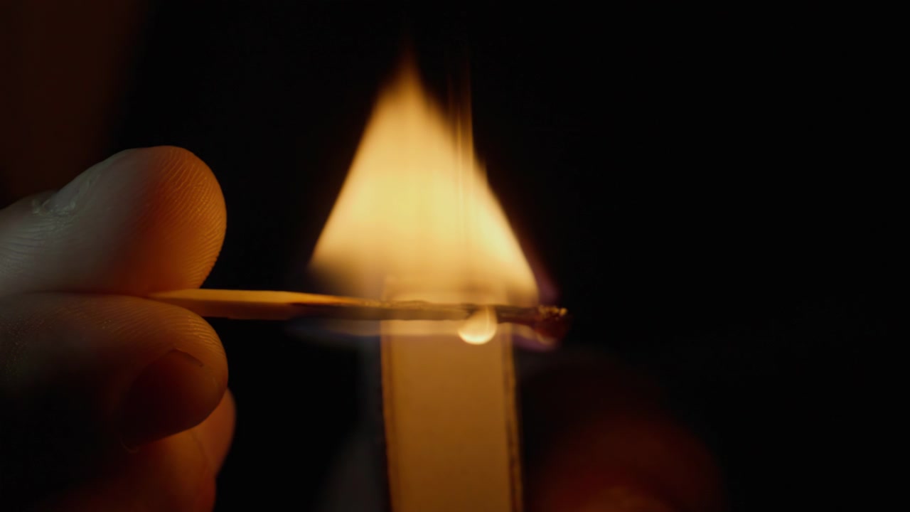Primo piano di una mano che tiene un fiammifero acceso e spegne la fiamma su sfondo nero isolato