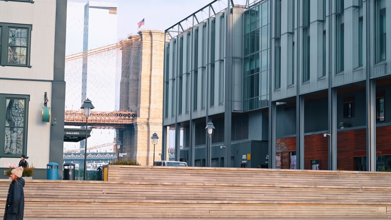 New York, USA, 5 dicembre 2025: terrazza in legno a gradoni con vista sul ponte di Brooklyn. Vista da una terrazza in legno a gradoni che mostra un moderno edificio commerciale con la torre in pietra del ponte di Brooklyn visibile tra le strutture