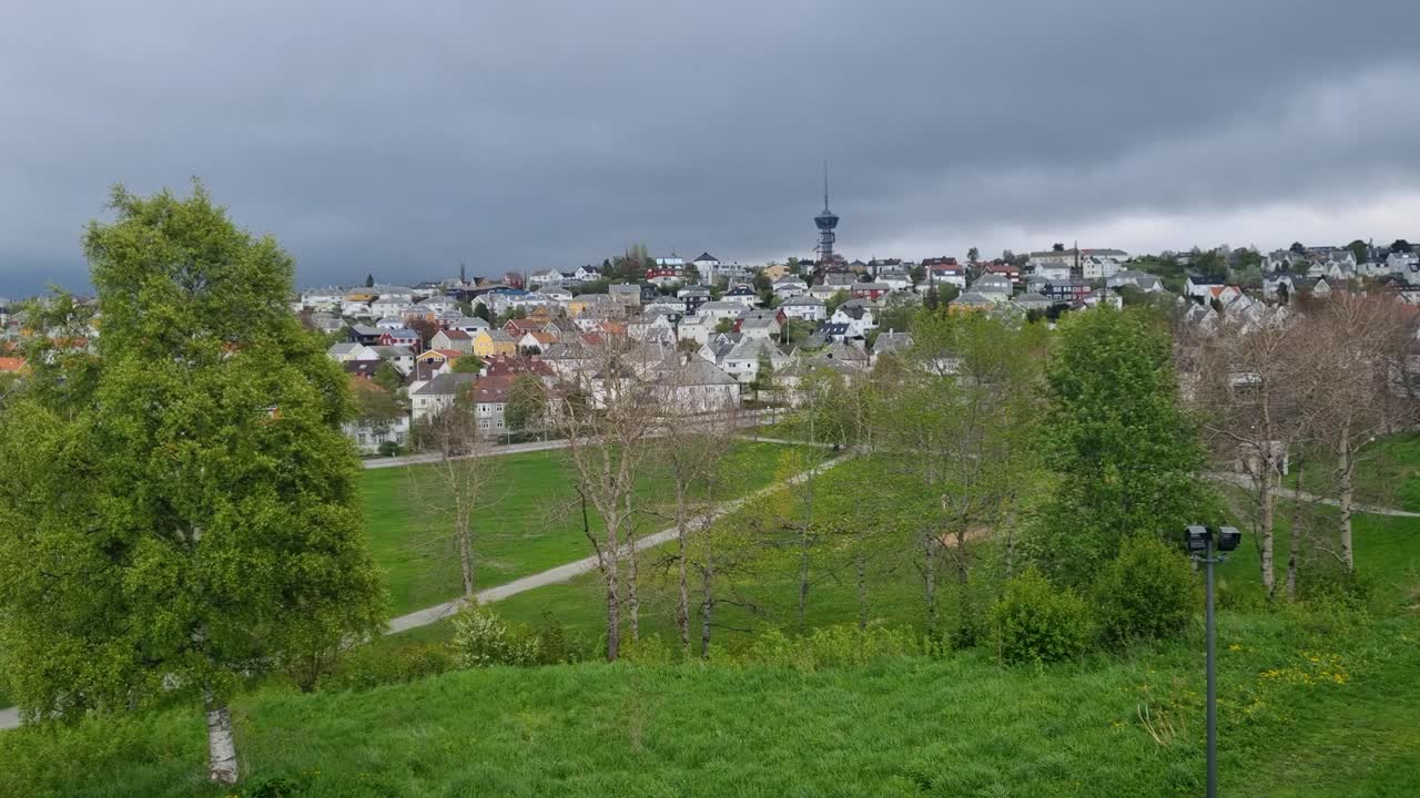 Panoramic shot of the Tyholt district in Trondheim, Norway, on a cloudy spring day, highlighting the TV tower atop a lush green hill and the surrounding neighborhood