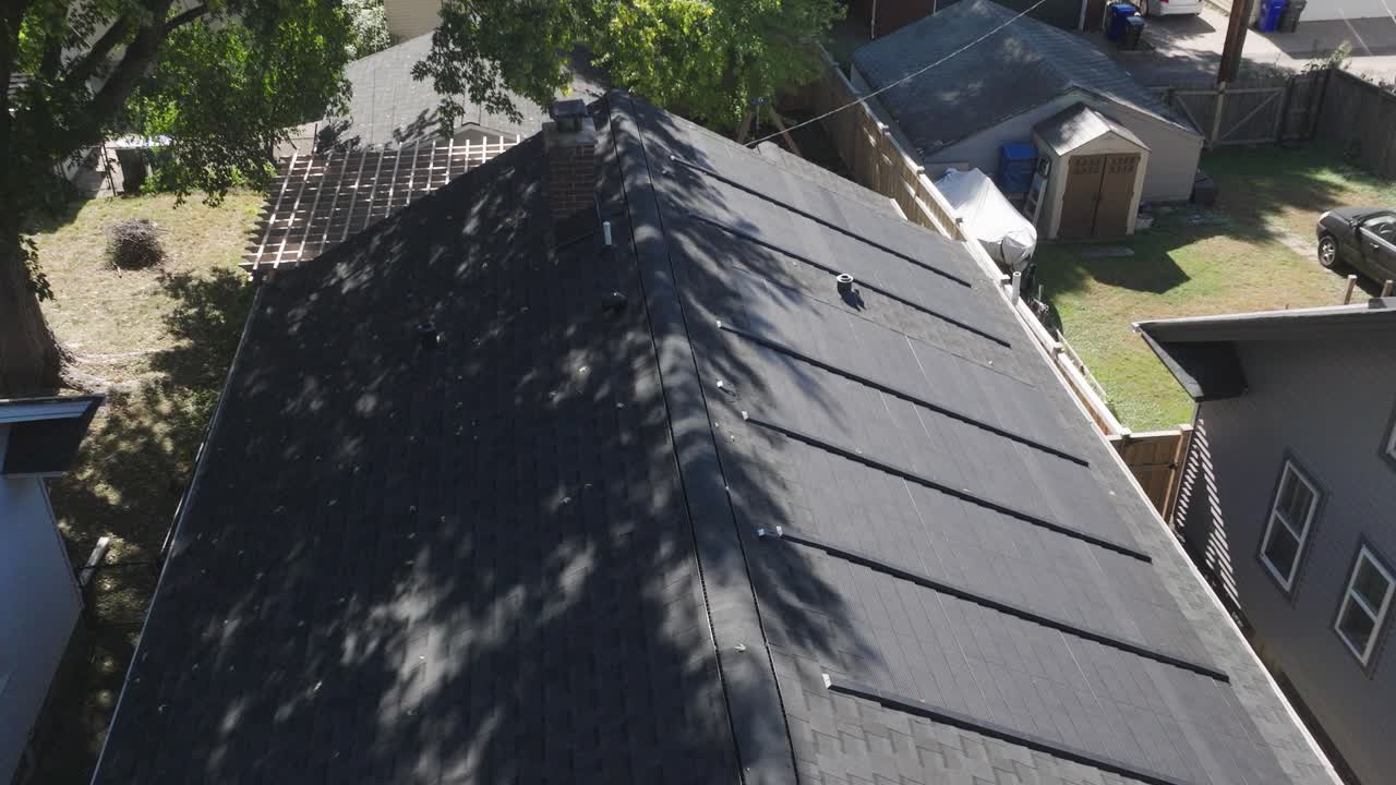 una vista de drones de arriba hacia abajo de tejas solares instaladas en un techo residencial sombreado por árboles.