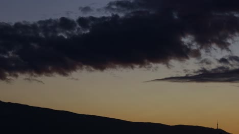 timelapse of moving clouds above a mountain's silhouette, at dusk