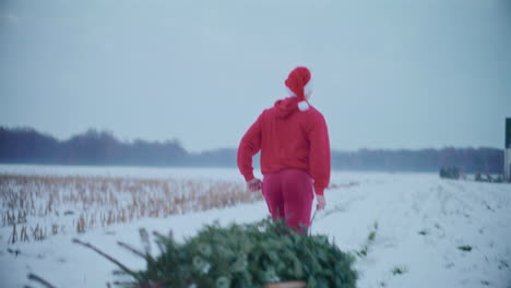 Glücklicher-Mann-Zieht-Weihnachtsbaum,-Während-Er-Durch-Eine-Schneebedeckte-Landschaft-Läuft