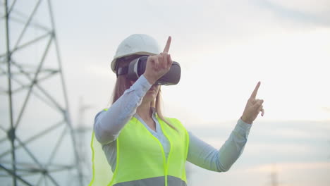 middle plan female energy engineer in virtual reality glasses and white helmet on the background of high-voltage power line towers