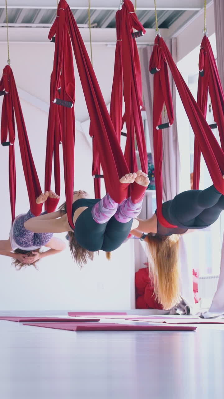 barefoot ladies lie relaxed in special bright red hammocks after aerial fly yoga lesson in modern fitness room