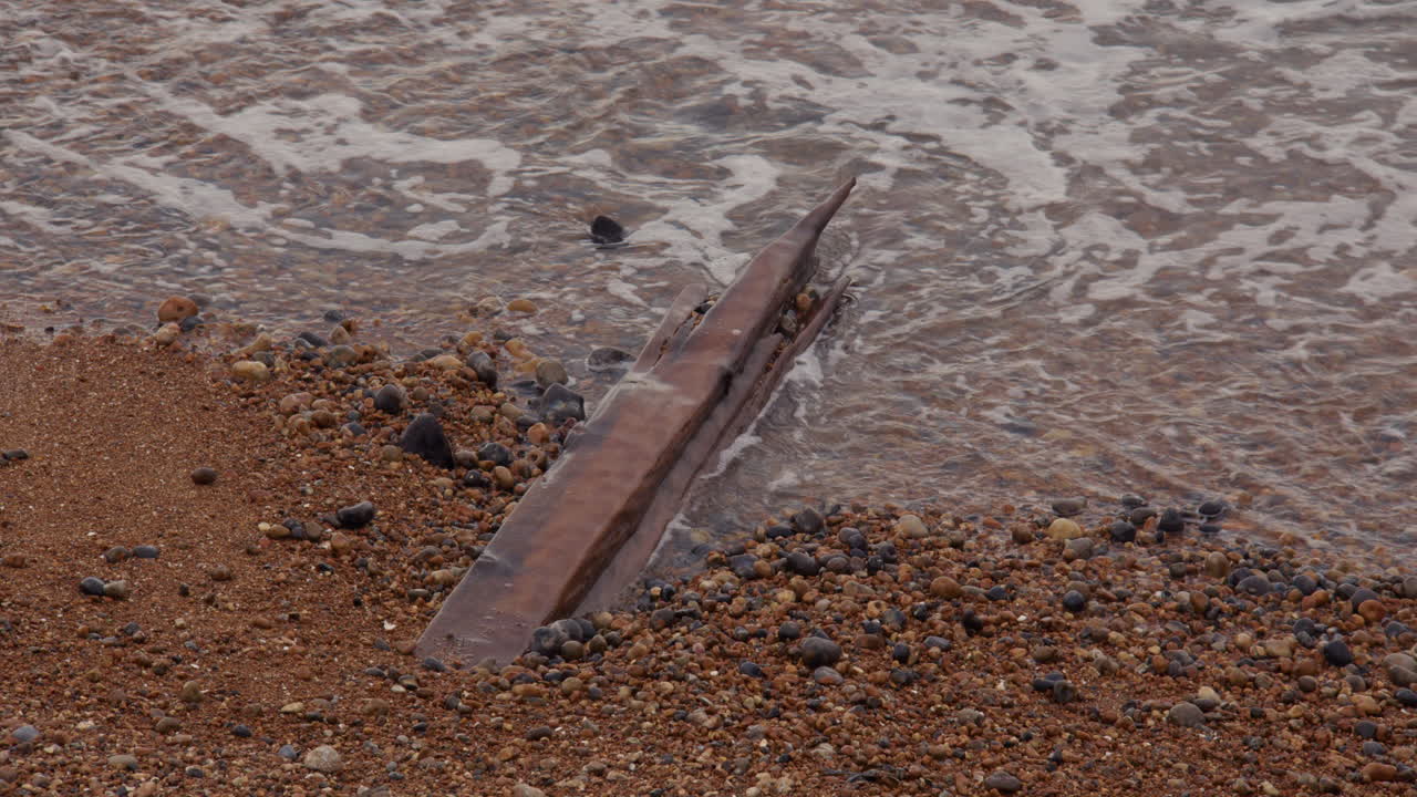 Ampia inquadratura di onde che lambiscono un vecchio pezzo di legno vicino al porto di Shoreham