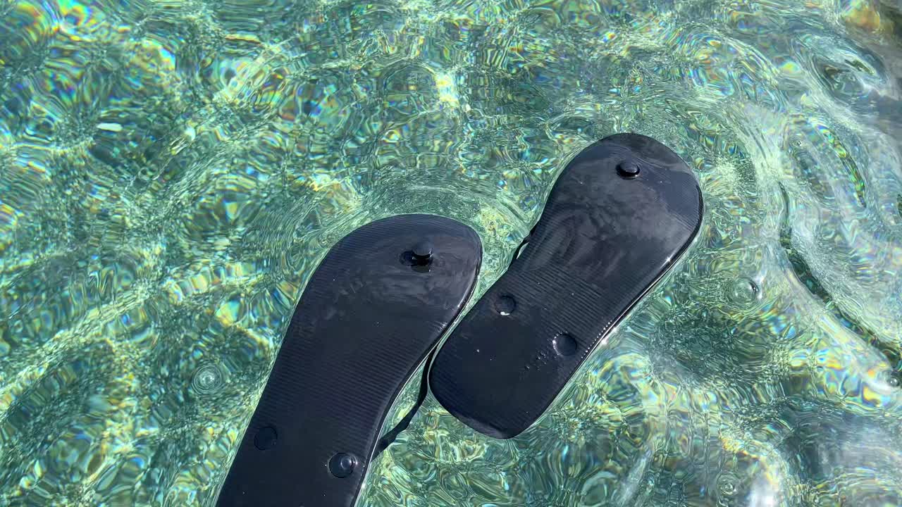 flotando negras zapatillas al revés en transparente agua de mar turquesa por la playa en españa, divertido vacaciones de verano soleadas zapatos de vacaciones, tiro de 4k
