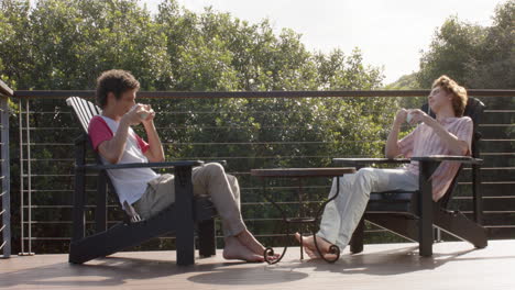 happy diverse gay male couple drinking coffee on balcony at home, slow motion