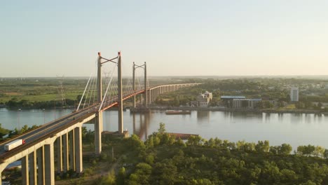 Toma-Aérea-Volando-Junto-A-Un-Puente-Atirantado-Que-Cruza-Un-Gran-Río-A-La-Hora-Dorada