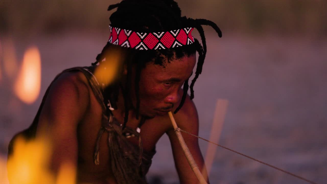 retrato en primer plano de la gente de san (bushmen) tocando un instrumento musical tradicional al atardecer alrededor de un fuego
