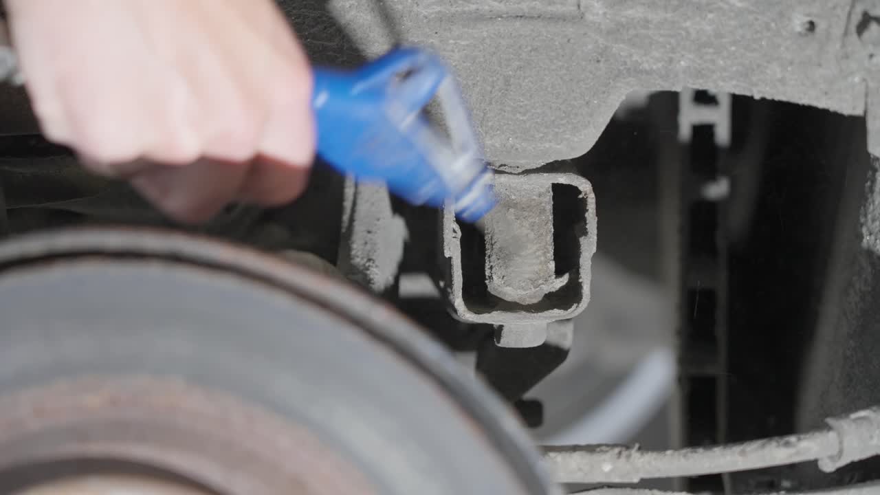 Person using compressed air gun to blow dirt and grime from car under body behind rear brakes, close up