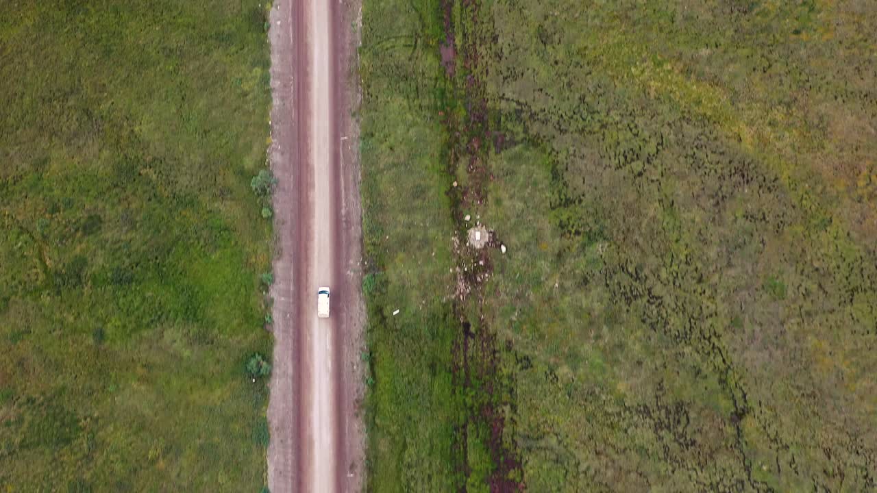 알래스카 풀이 무성한 야생 지형을 통해 흙길을 달리는 흰색 미니밴 - 공중 하향식 추적 샷