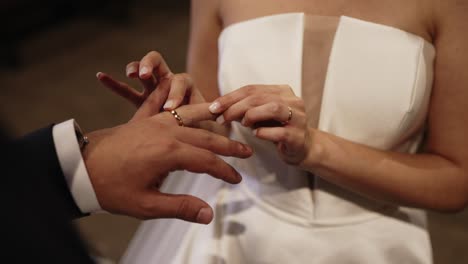 bride in white dress gently placing a gold wedding ring on groom's finger during ceremony
