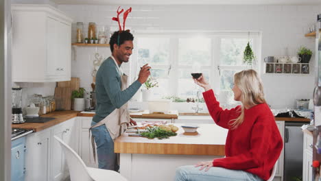 couple wearing fancy dress antlers making a toast whilst preparing dinner on christmas day