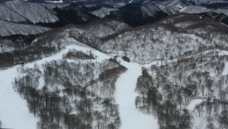 snow capped mountain peaks with skiers in winter at nozawa japan in nagano region, aerial