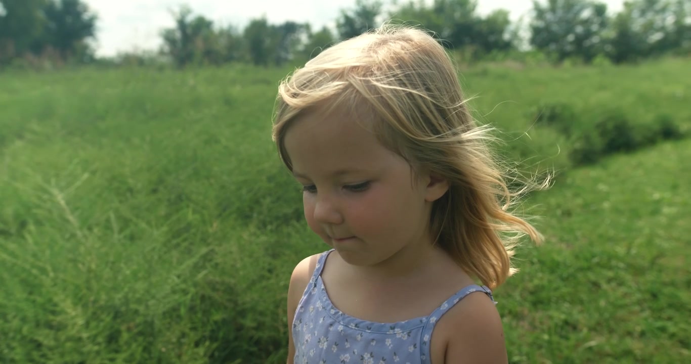 A closer perspective of a young girl walking through grass, focusing on her movement and environment.