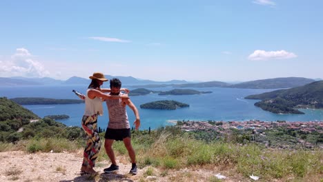 a young couple hugs and poses at a viewpoint above the town of nidri, greece