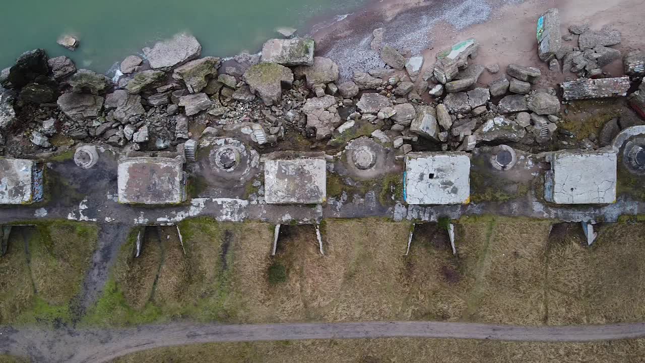 Aerial birdseye view of abandoned seaside fortification building at Karosta Northern Forts on the beach of Baltic sea in Liepaja in overcast spring day, drone shot moving right