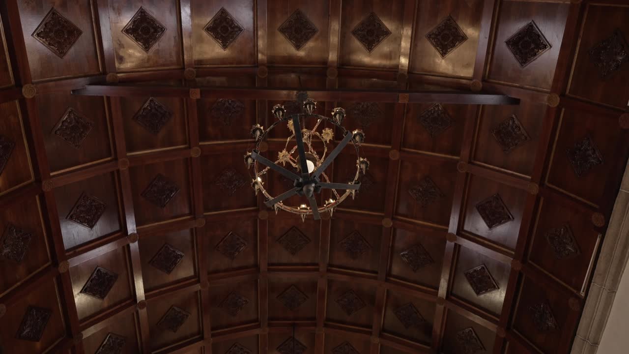 Ornate wooden ceiling with a central chandelier, featuring intricate geometric carvings