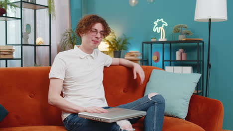 happy caucasian man sitting on couch closing laptop and relaxing after finishing work in living room