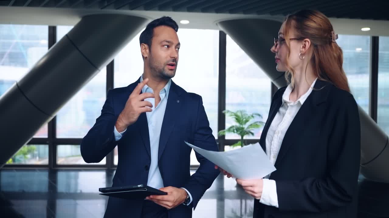 Two business people, man and woman, discussing documents in bright modern office setting walking and talking in agreement
