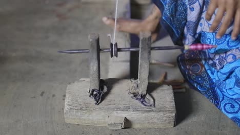 primer plano de una herramienta utilizada por una mujer en sari azul sentada en el suelo en sri lanka usando el hilo tejido hecho a mano para coser ropa