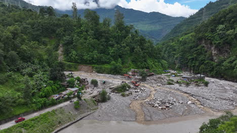 drone shot captures greenery of sindhupalchowk, nepal, with devastation caused by river floods. jcb machines work to manage destruction of homes, as villagers face a sad and challenging time